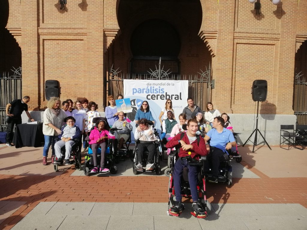 Un grupo de personas con parálisis cerebral celebra el Día Mundial de la Parálisis Cerebral delante de una pancarta que anuncia el día